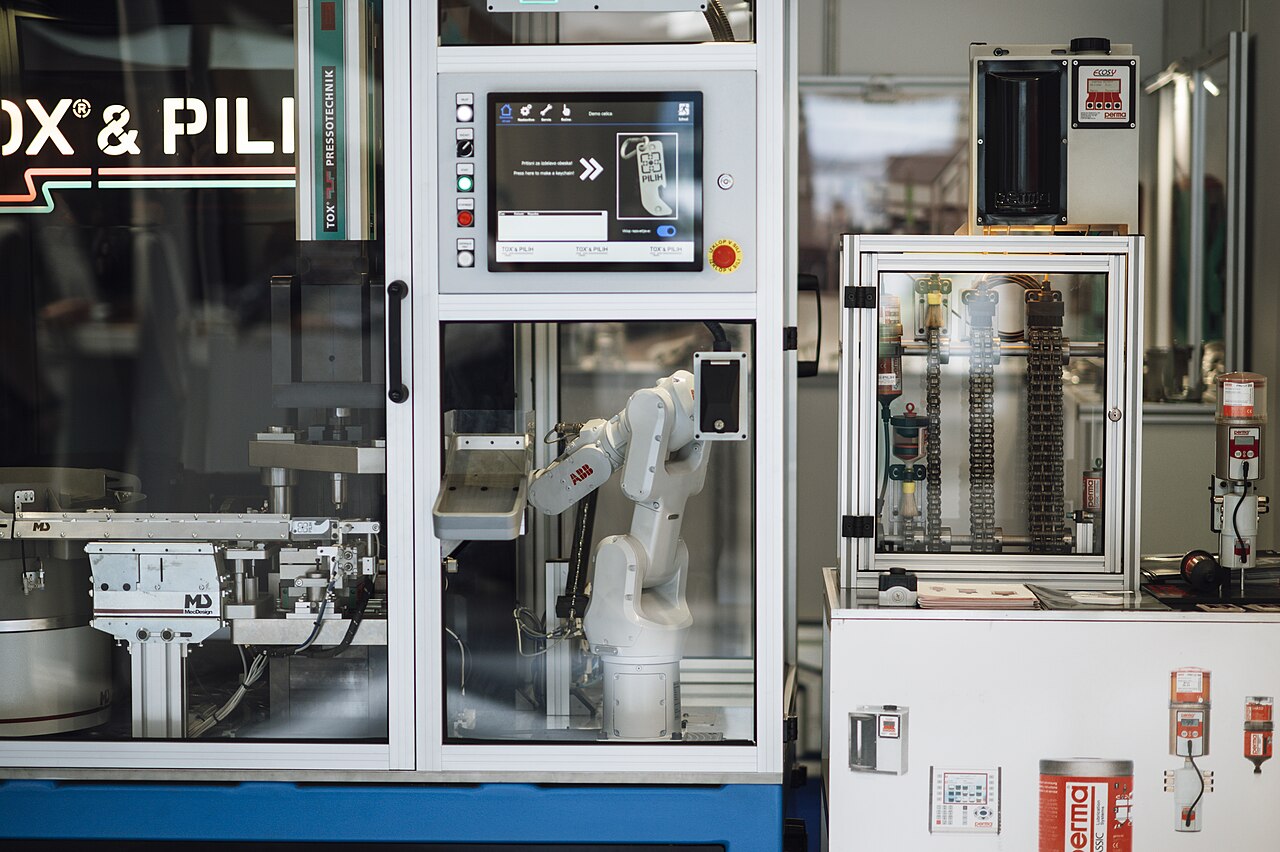 An industrial robotic arm working with machinery behind a protective enclosure
